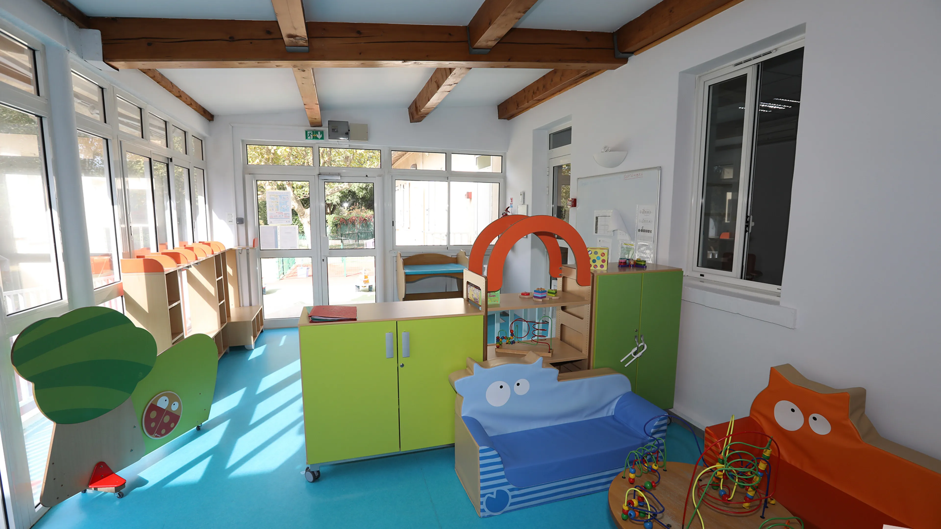 Photographie de l'intérieur d'une salle de crèche, les meubles et le sol sont colorés, on peut y observer des bancs, des meubles et des activités d'intérieur conçus pour les bébés