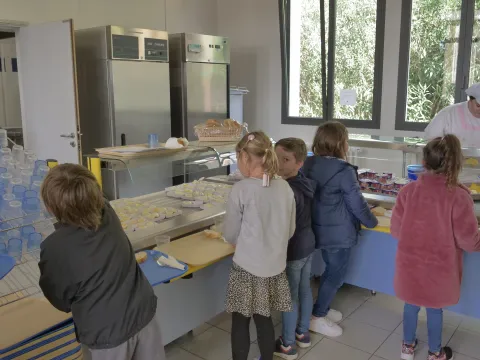 Photographie d'un groupe d'enfants de dos se servant à la restauration scolaire de leur établissement