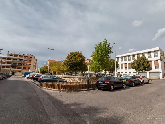 Vue sur la place arborée où des véhicules sont stationnés.