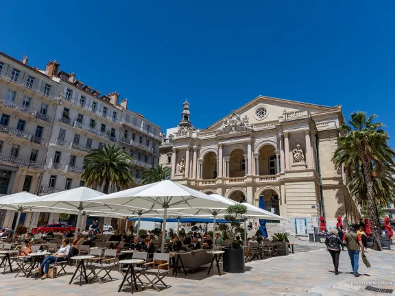 Opéra dans le fond avec devant lui une terrasse de café et des palmiers sur les côtés