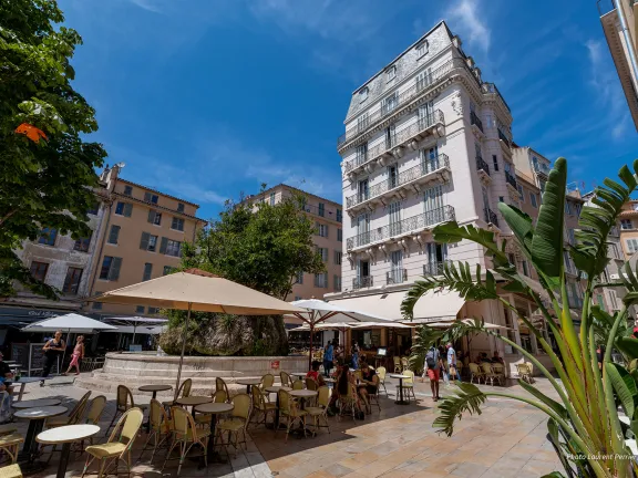 Place avec terrasses de café et en son centre une fontaine avec un grand arbre