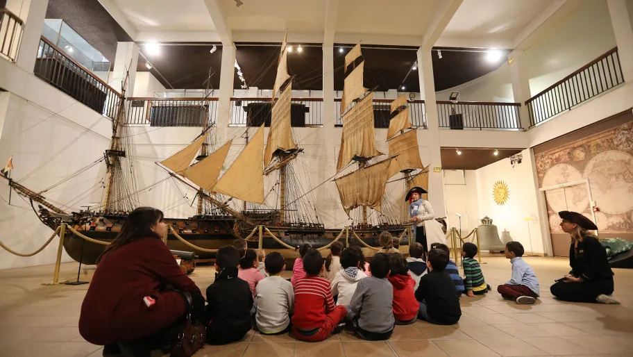 Photo d'un groupe d'enfants assis en intérieur observant une maquette de voilier