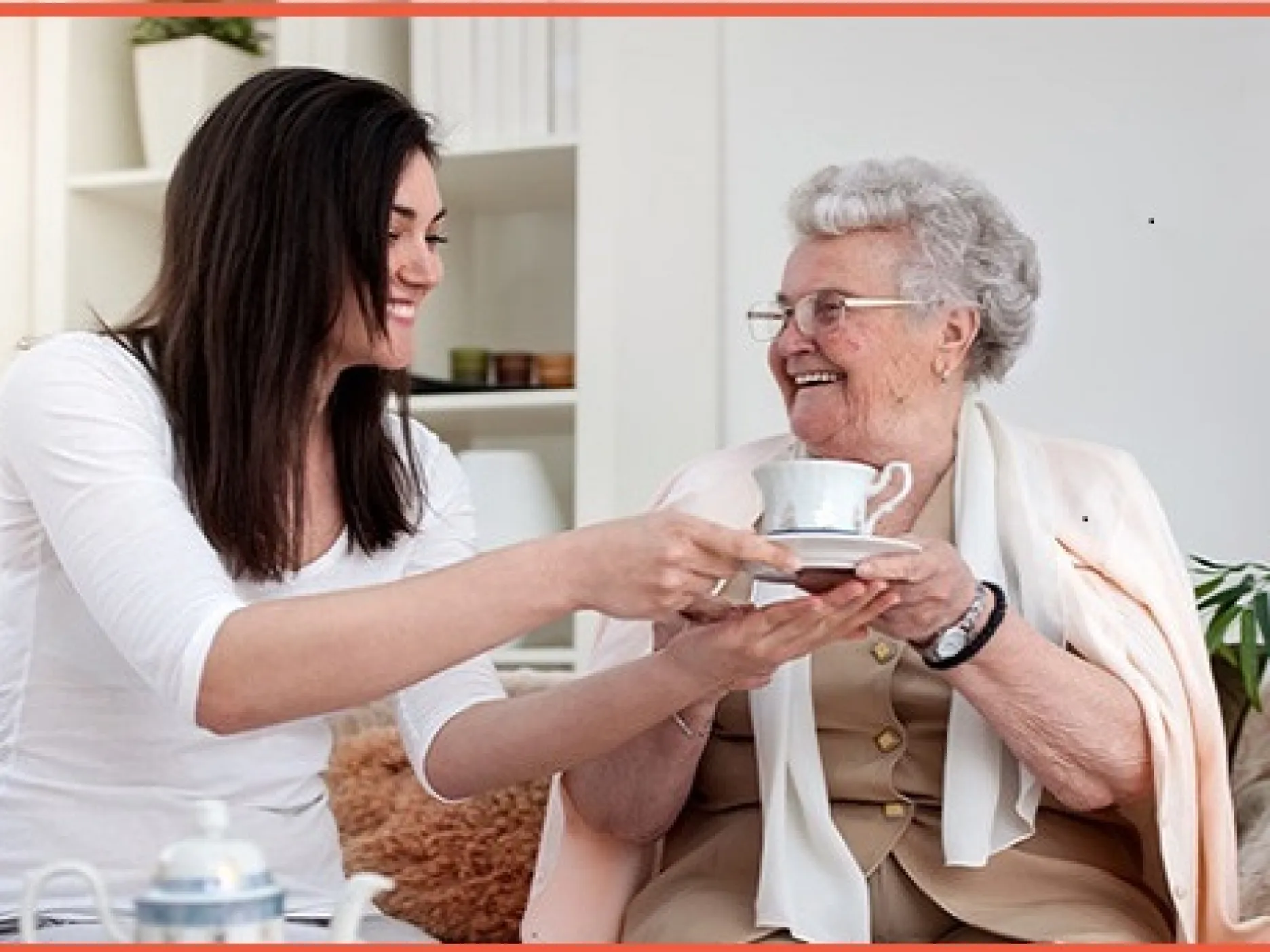 Une jeune femme tend une tasse de thé à une personne âgée assise dans son canapé