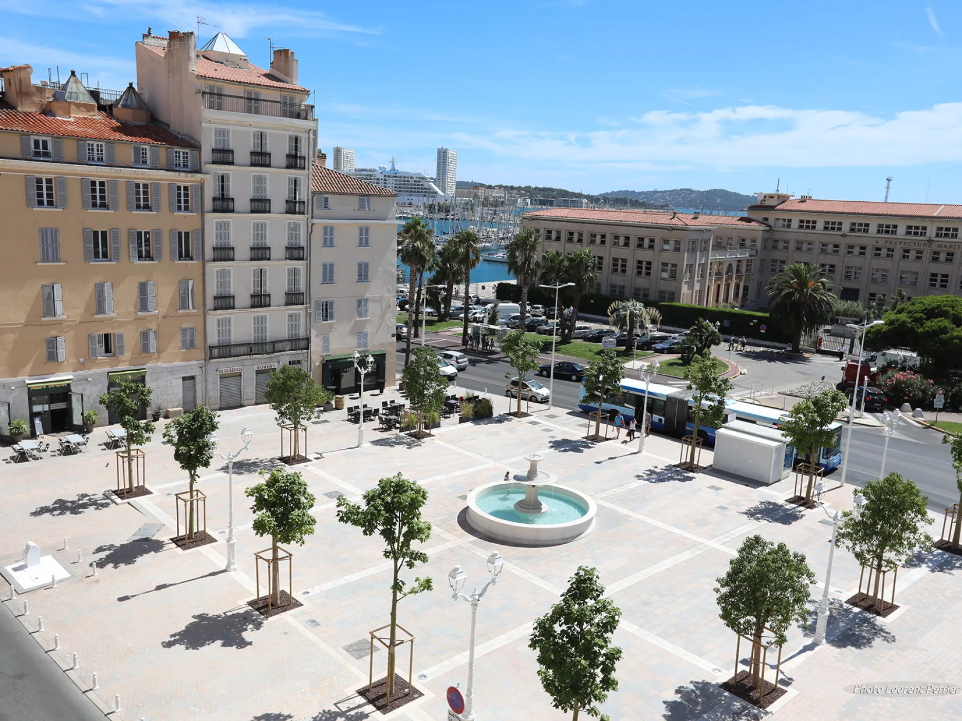 Vue aérienne de la place avec des arbres encadrant la place avec au milieu une fontaine.