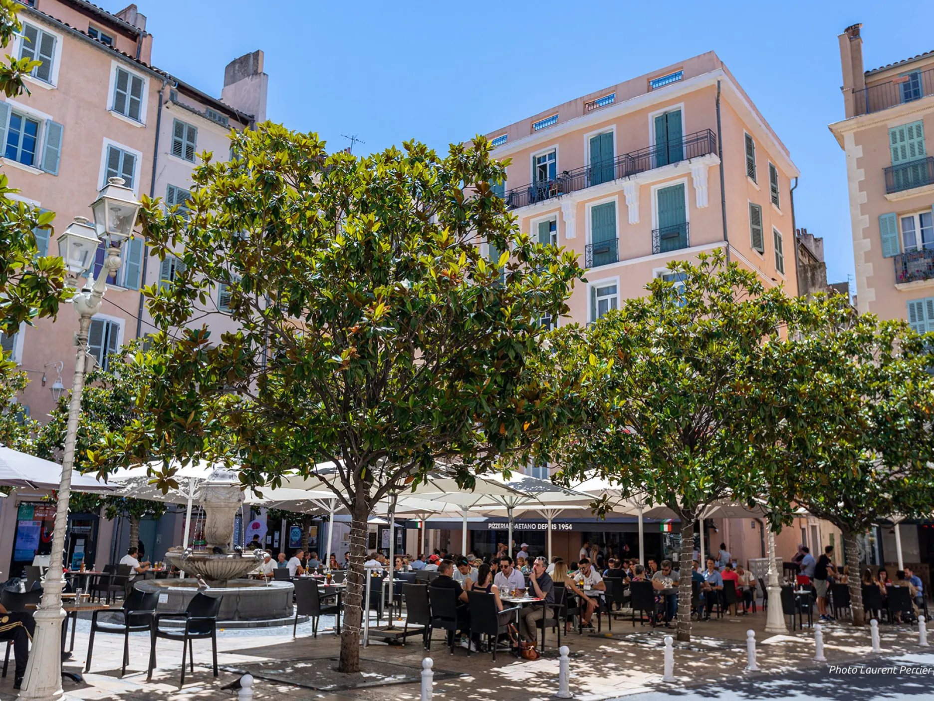 Fontaine au centre, entourée de terrasses de cafés et d'arbres